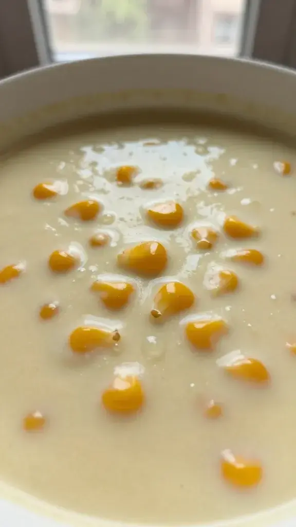 Close-up detail of the corn soup’s creamy texture with kernels visible, tiny droplets of broth, soft shallow focus, warm natural window light