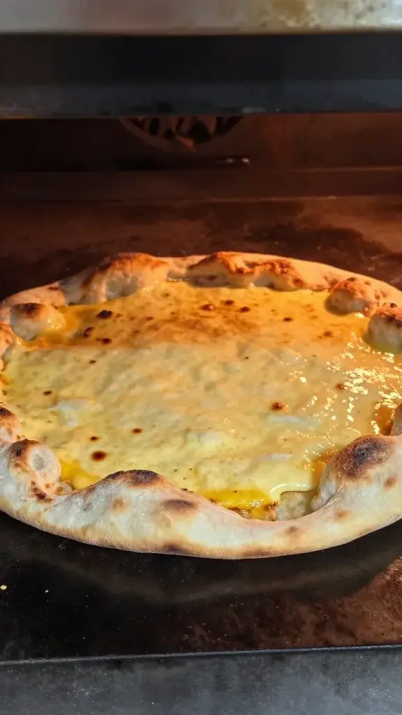 Cooking process shot: painterly close-up of flatbread sliding into a hot oven, cheese starting to melt, crisp crust forming, soft interior glow from oven light
