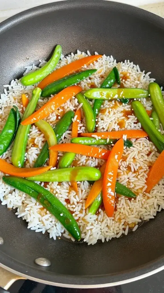 Cooking process shot of sautéed veggies, rice sizzling in a pan with a splash of soy glaze, glossy finish on vegetables, natural kitchen light, motion of stirring